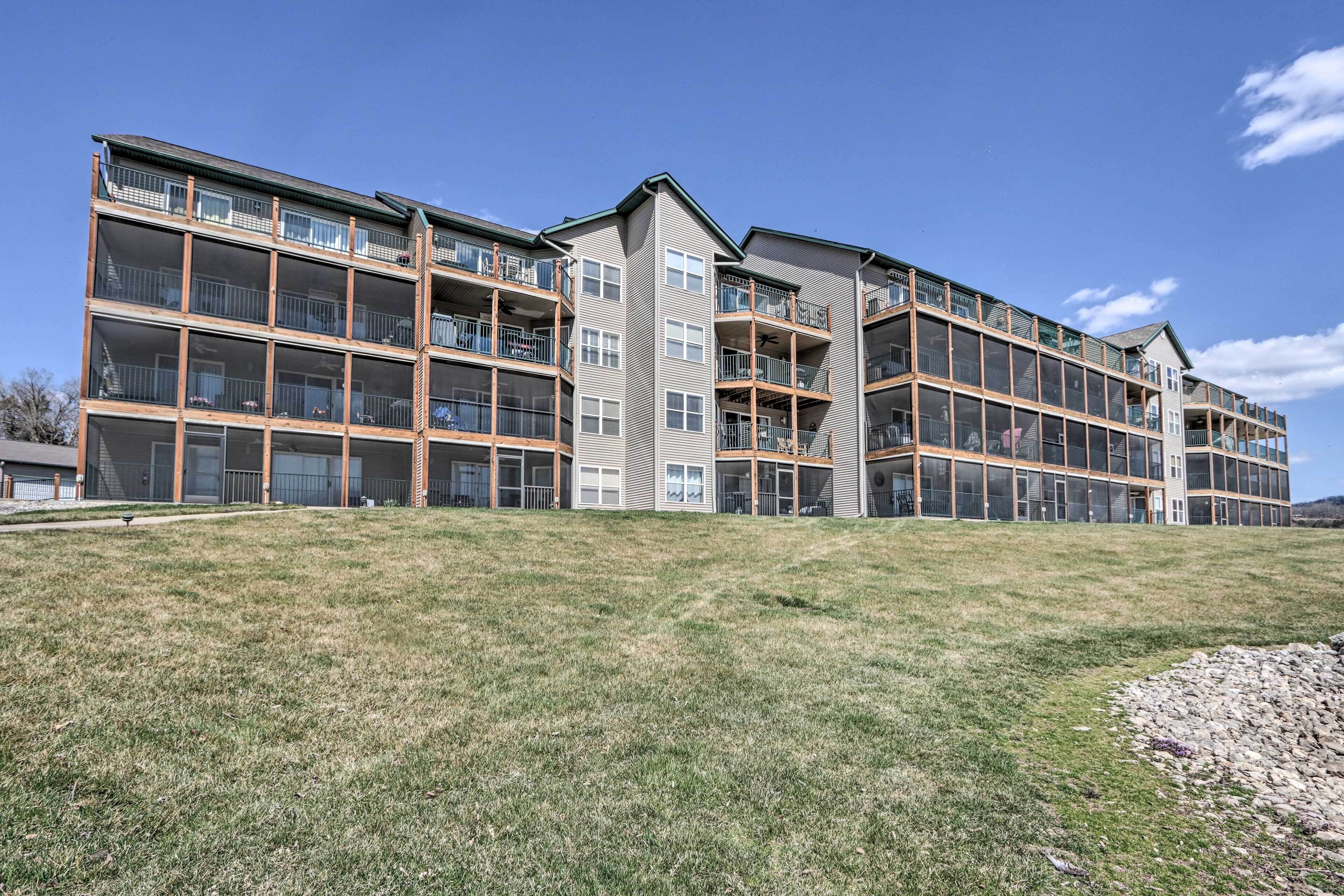 A multi-story residential building with balconies, large windows, and a grassy area in front.