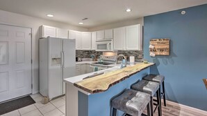 Una cocina moderna con armarios blancos, una isla de madera con taburetes de bar, un microondas y un lavamanos.