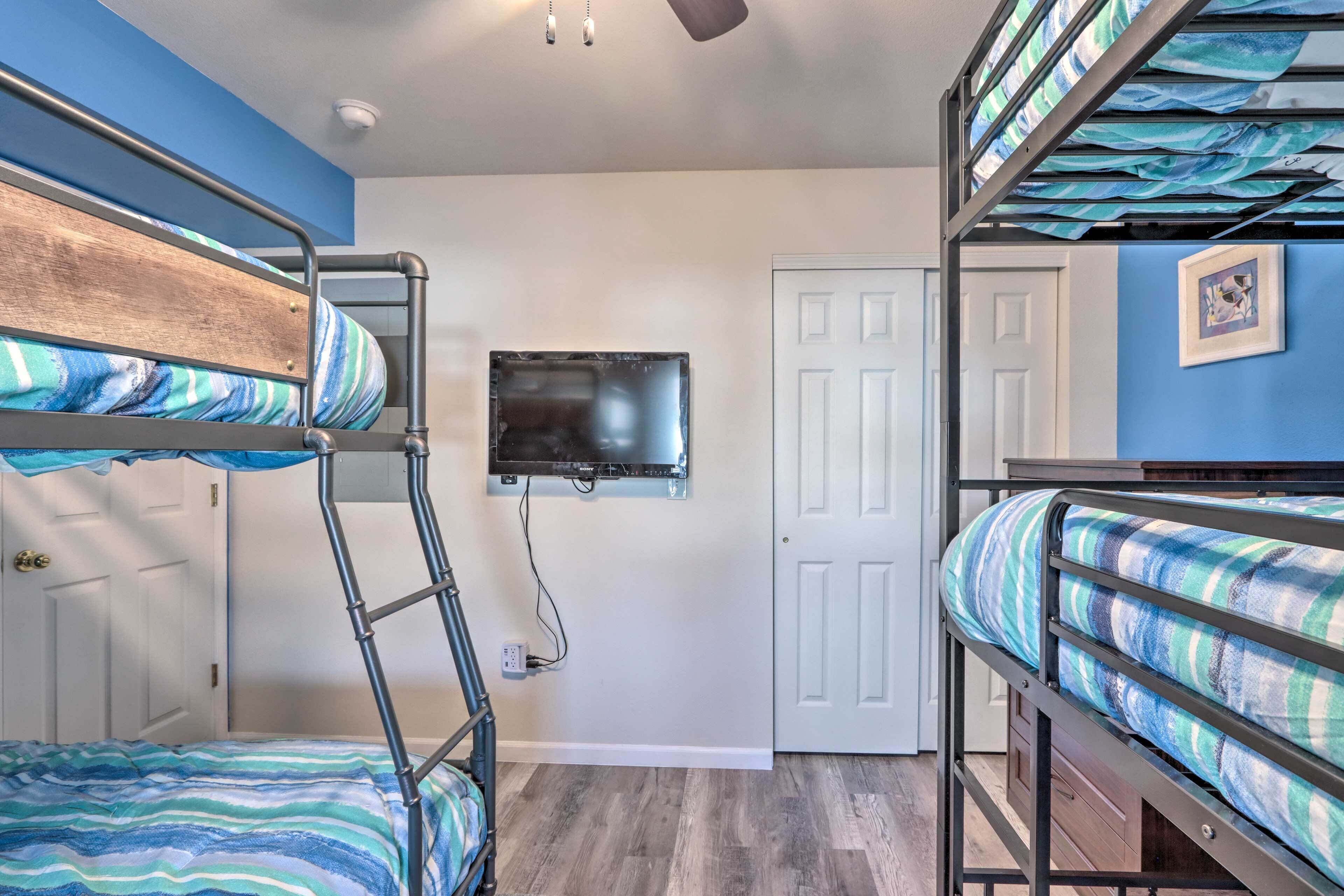 A bunk bed room with a television mounted on the wall, a door, and a framed picture on the wall.