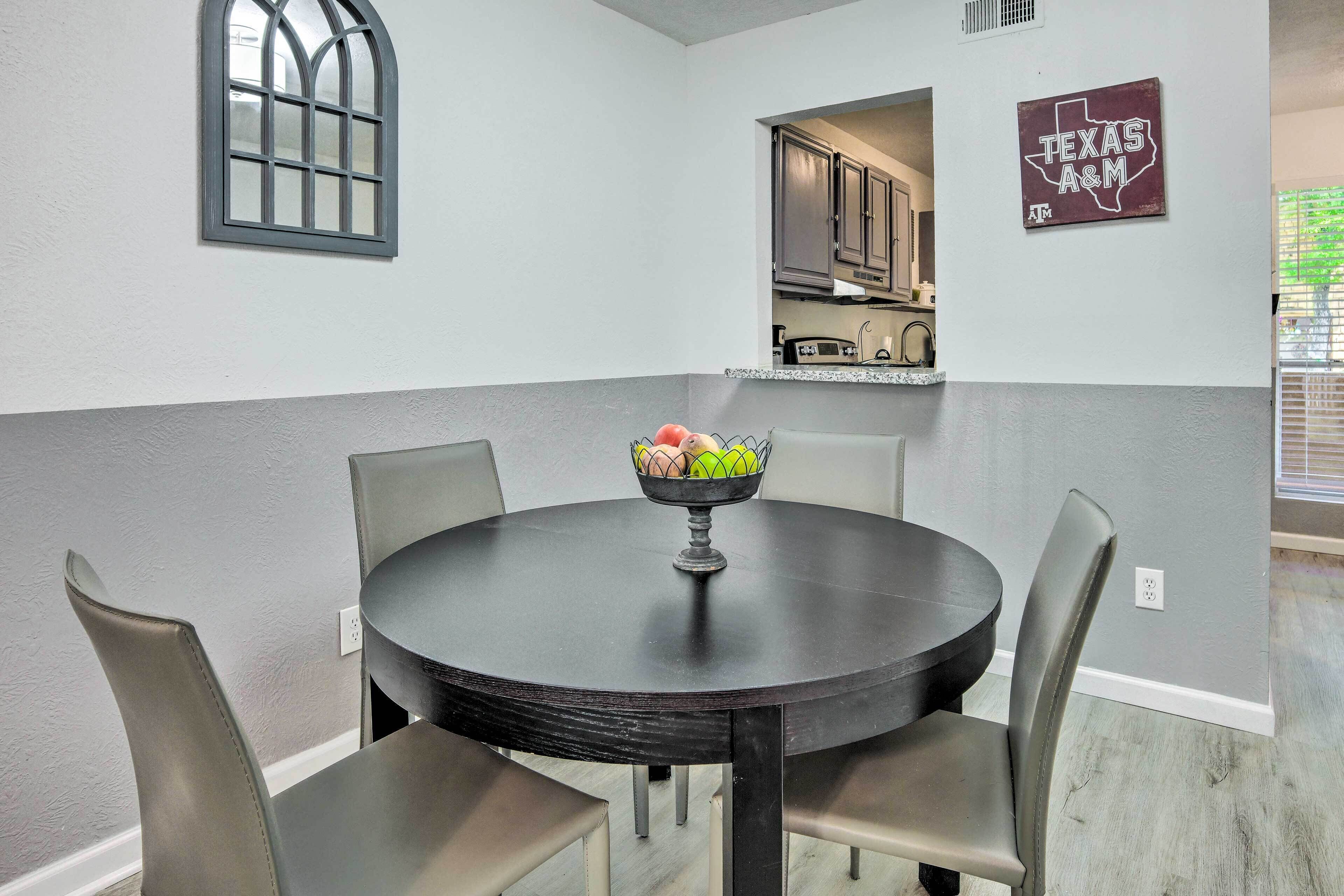 A dining area with a round table, four chairs, and a bowl of fruit.