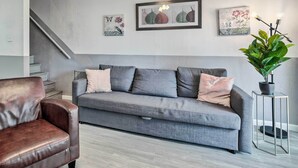 A living room with a grey sofa, a brown leather chair, and a potted plant. There are framed artworks on the wall and a staircase in the background. - Pet-friendly Bryan Escape ~ 2 Mi to Texas A & M (Bryan)