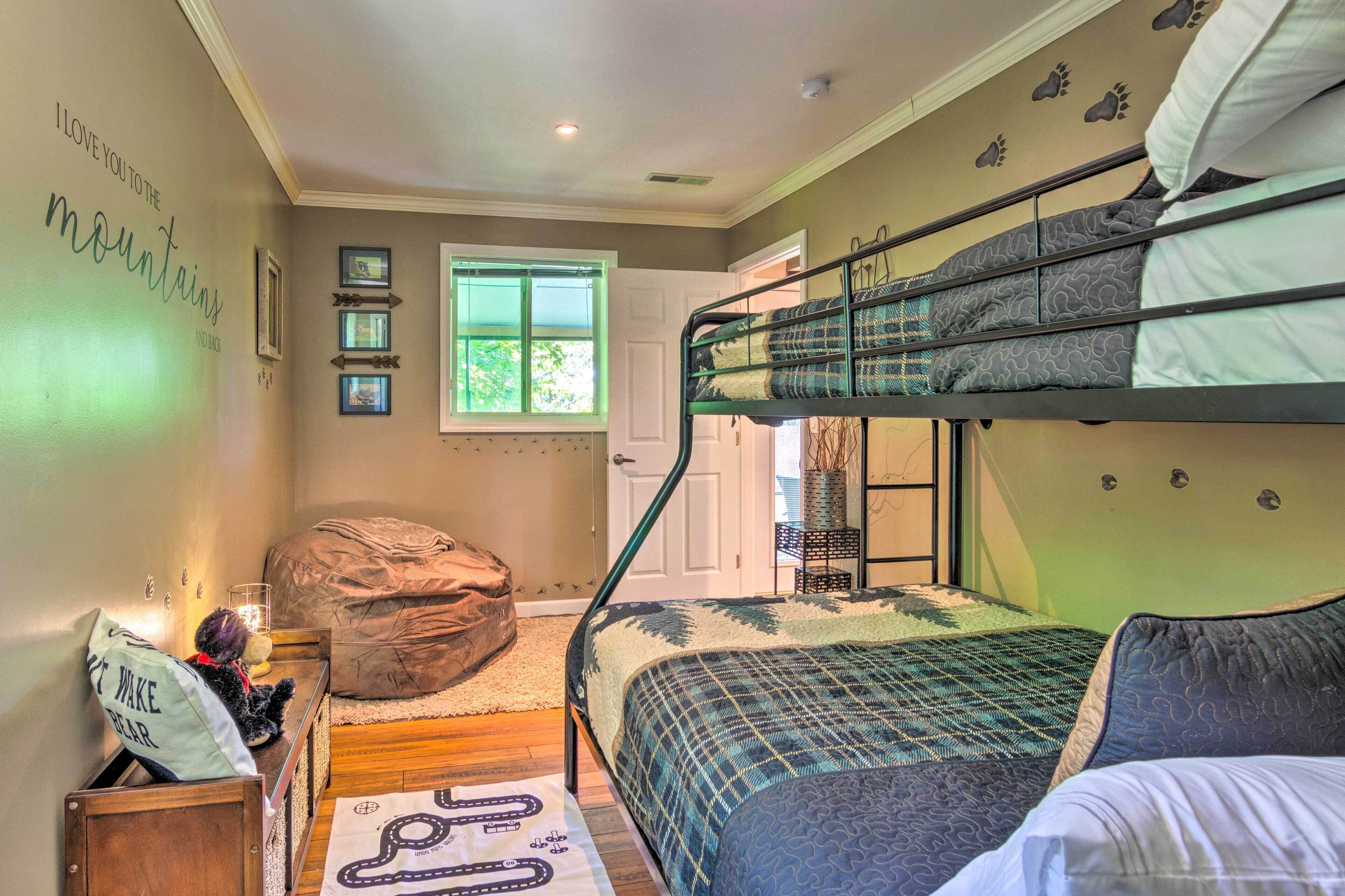 A bunk bed room with a window, a bean bag chair, a small table with a teddy bear, and a wall with a mountain-themed sign.