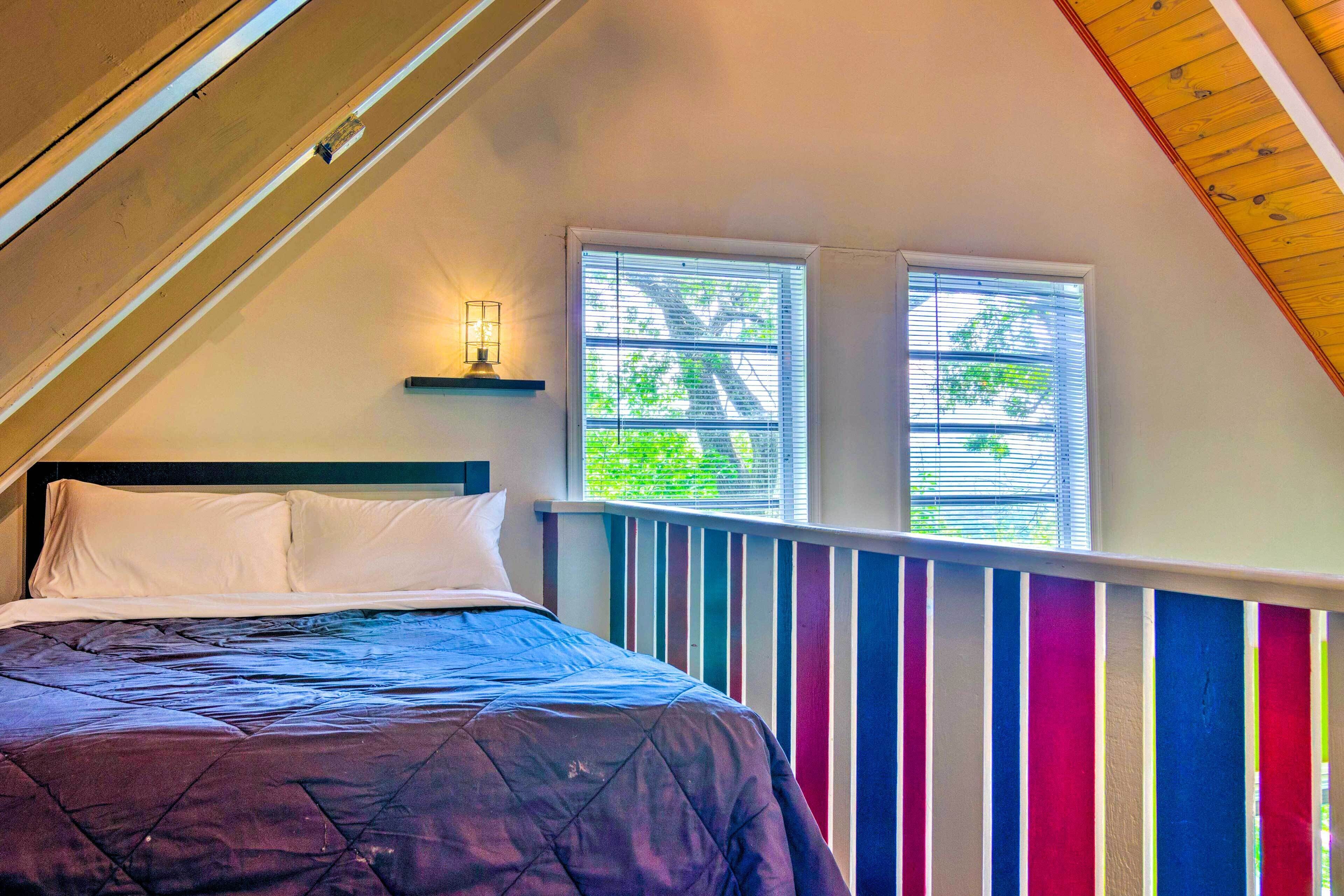 A bedroom with a bed, a nightstand, a window with blinds, and a sloped ceiling.