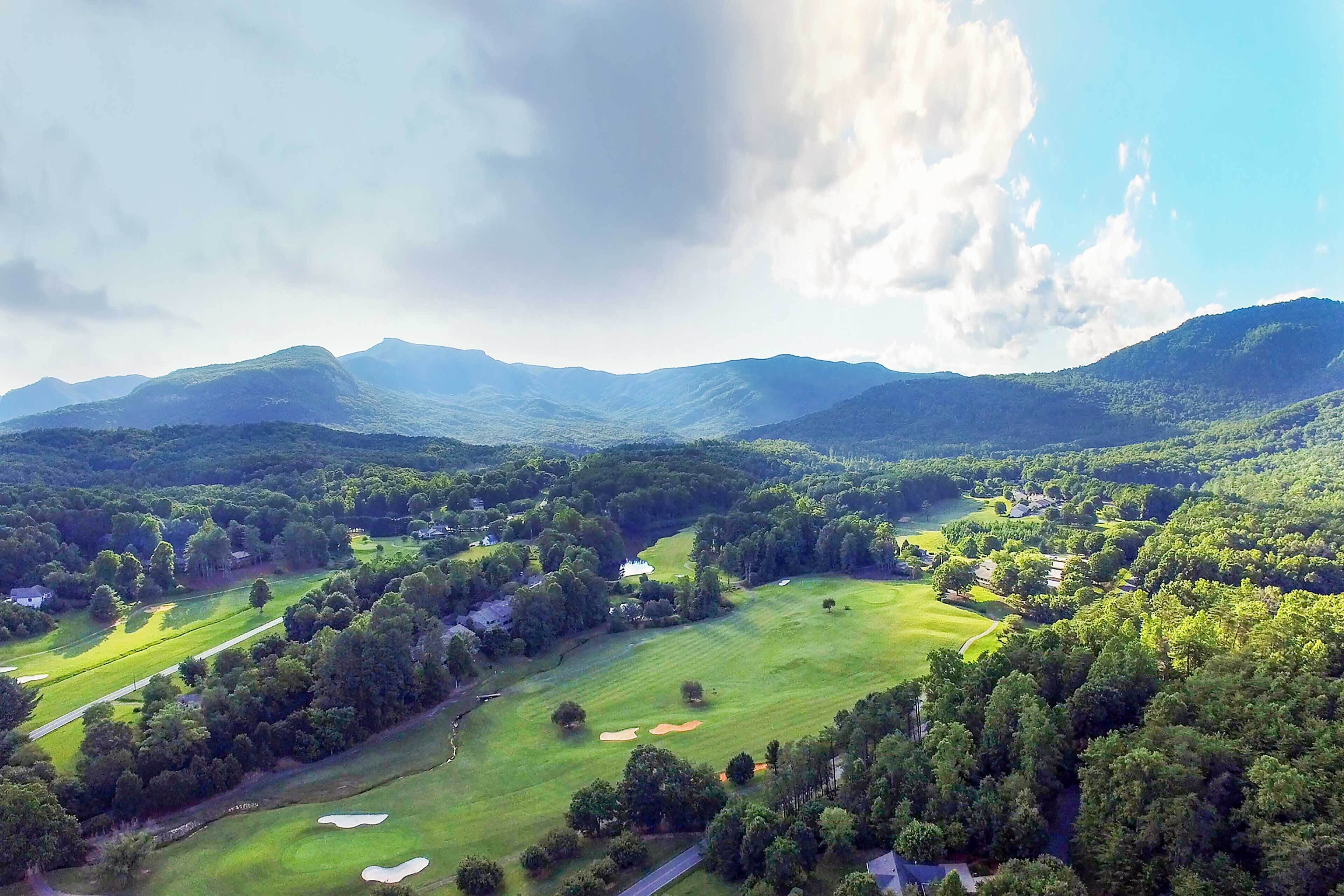 A golf course with multiple holes, surrounded by dense forests and rolling hills.