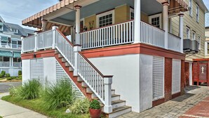 Ein zweistöckiges Haus mit weißer Fassade, rotem Sockel und einer Holztreppe, die zu einem Balkon führt.