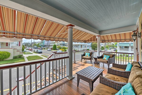 A covered outdoor area with wicker furniture, a wooden table, and a view of a residential street.