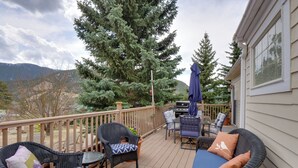 Eine Terrasse mit Korbmöbeln, einem Grill und Blick auf die Berge.