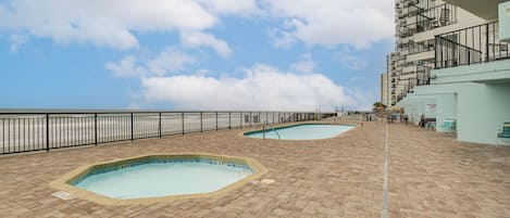 A rooftop pool area with two pools, a metal railing, and a staircase leading to an upper level.
