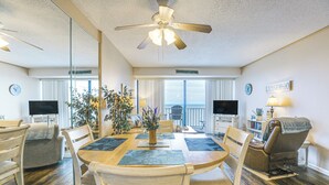 A spacious room with a dining table, chairs, a ceiling fan, and a view of the outdoors. - Oceanfront Garden City Beach Condo For Families! (Murrells Inlet)