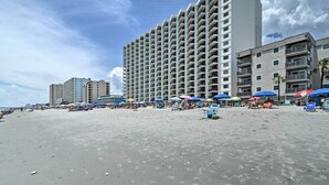 A beachfront hotel with multiple floors, beach umbrellas, and a sandy beach. - Oceanfront Garden City Beach Condo For Families! (Murrells Inlet)