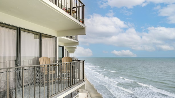 A balcony with a view of the ocean, a chair, and a table. - Oceanfront Garden City Beach Condo For Families! (Murrells Inlet)