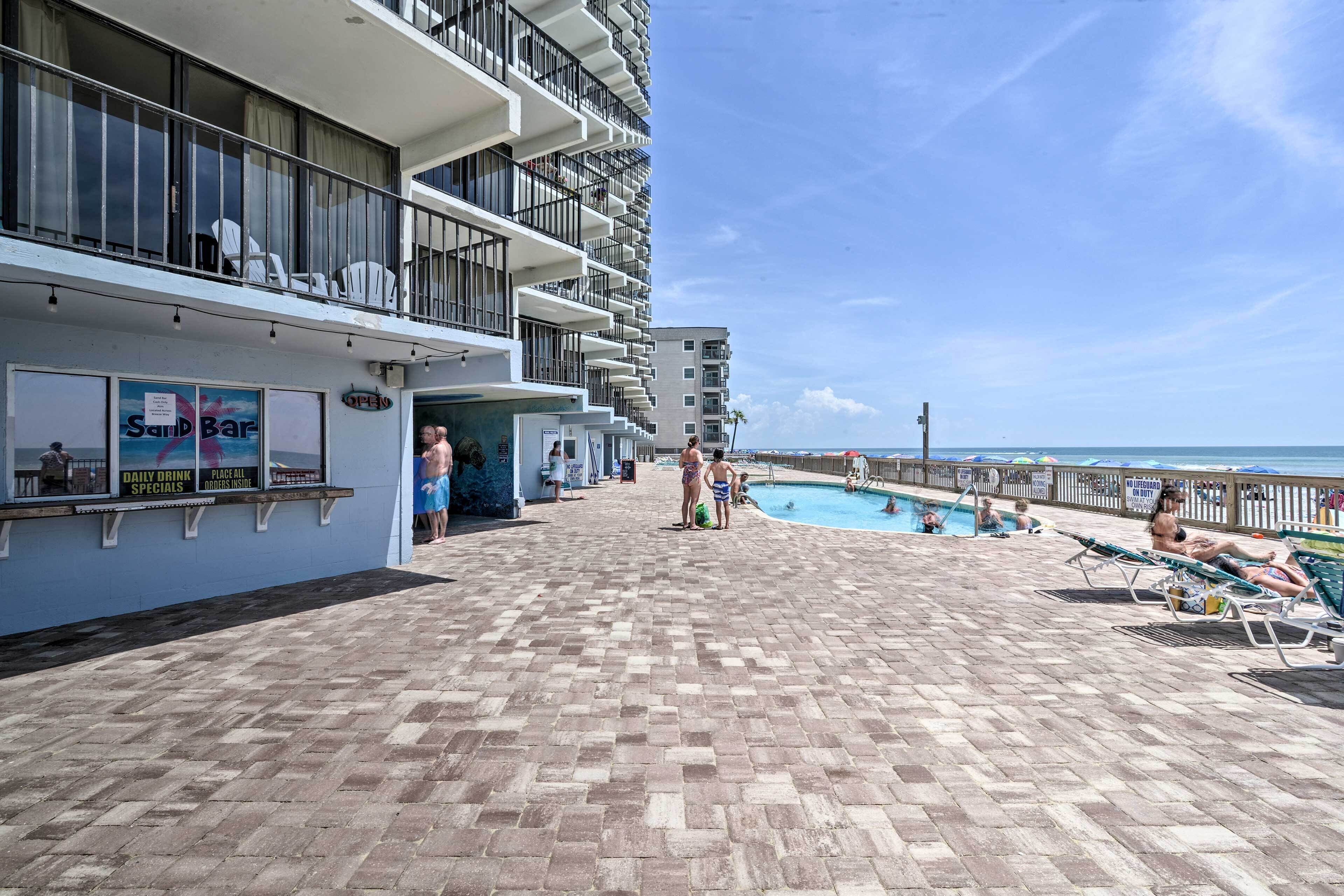 A poolside area with a bar, lounge chairs, and a view of the ocean.