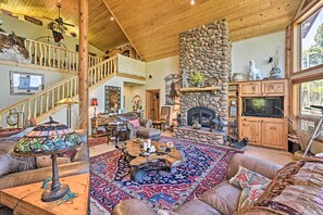 A spacious living room with a stone fireplace, a large wooden ceiling, and a cozy seating area with a patterned rug. - Angel Fire Mountain-view Retreat w/ Private Deck! (Angel Fire)