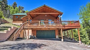 A wooden cabin with a covered porch, a garage, and a staircase leading to an upper level. - Angel Fire Mountain-view Retreat w/ Private Deck! (Angel Fire)