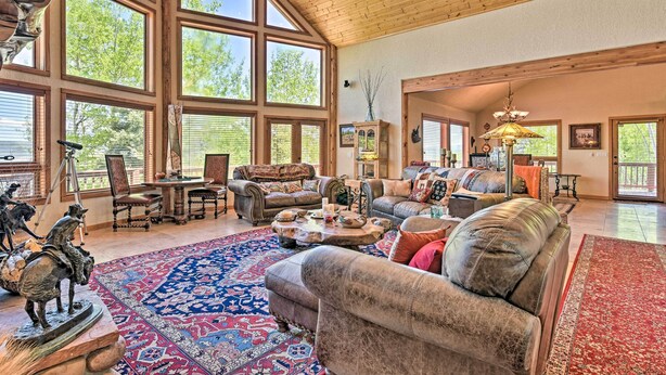 A spacious living room with large windows, a high wooden ceiling, and a mix of leather and fabric furniture. - Angel Fire Mountain-view Retreat w/ Private Deck! (Angel Fire)