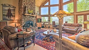 A spacious living room with leather sofas, a stone fireplace, and large windows offering a view of the outdoors. - Angel Fire Mountain-view Retreat w/ Private Deck! (Angel Fire)