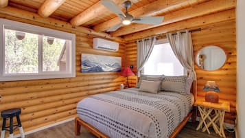 A log cabin bedroom with a bed, a ceiling fan, a window, and a wall-mounted air conditioner.