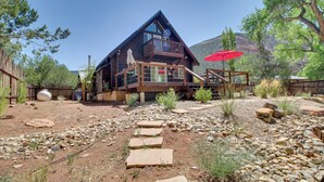 A rustic cabin with a balcony, surrounded by a rocky garden and a wooden deck.