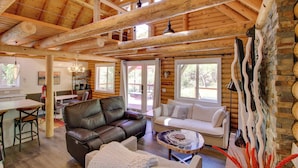 A log cabin interior with a dining area, leather seating, and a stone fireplace.