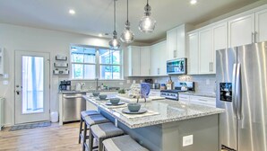 Una cocina moderna con una isla grande, electrodomésticos de acero inoxidable e iluminación colgante.