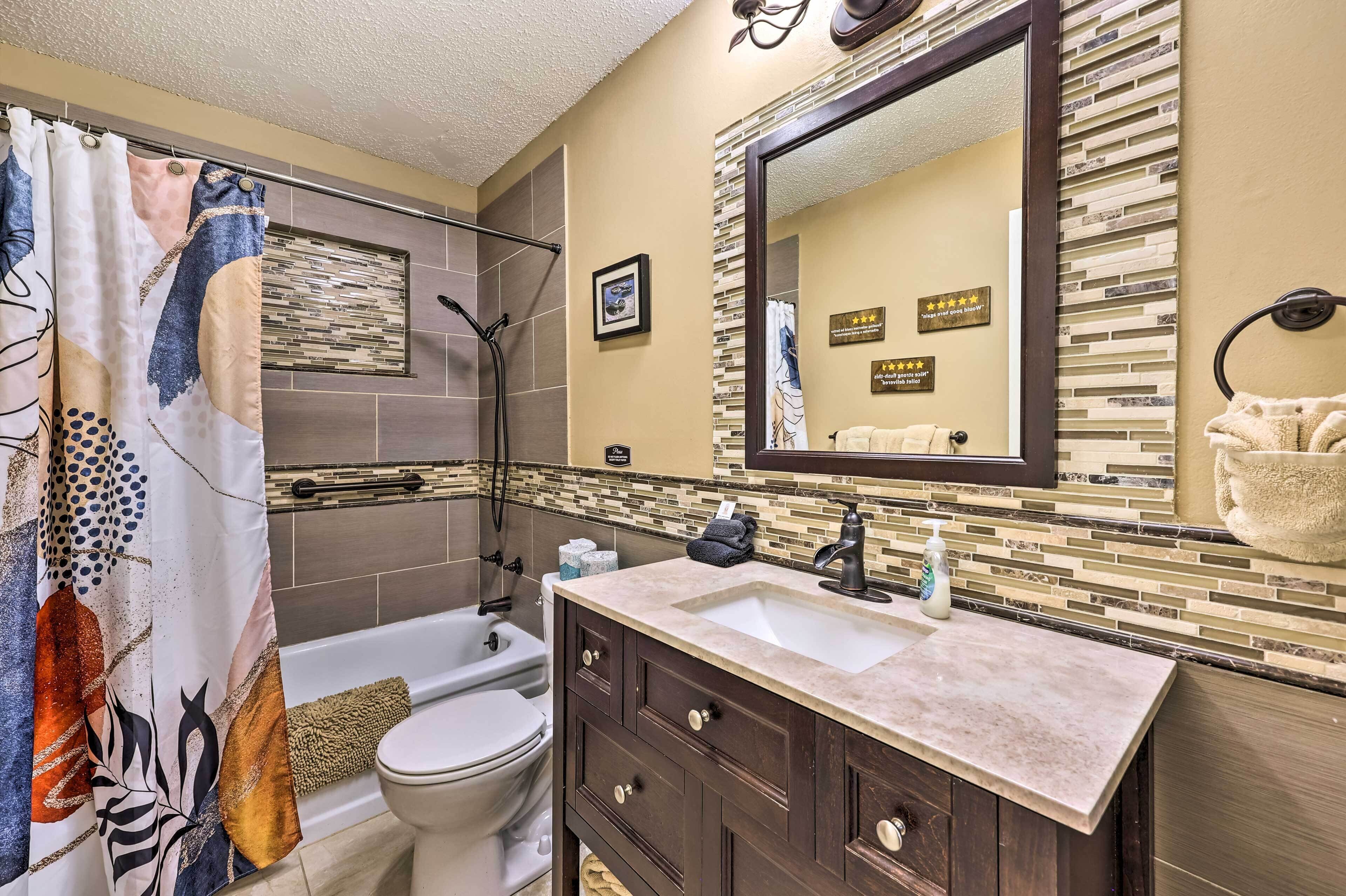 A bathroom with a shower curtain, a bathtub, a toilet, a sink with a mirror, and a towel rack.