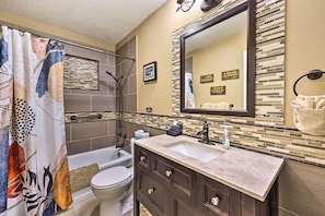 A bathroom with a shower curtain, a bathtub, a toilet, a sink with a mirror, and a towel rack. - Holiday Island Home: Hot Tub & Wood Stove! (Eureka Springs)