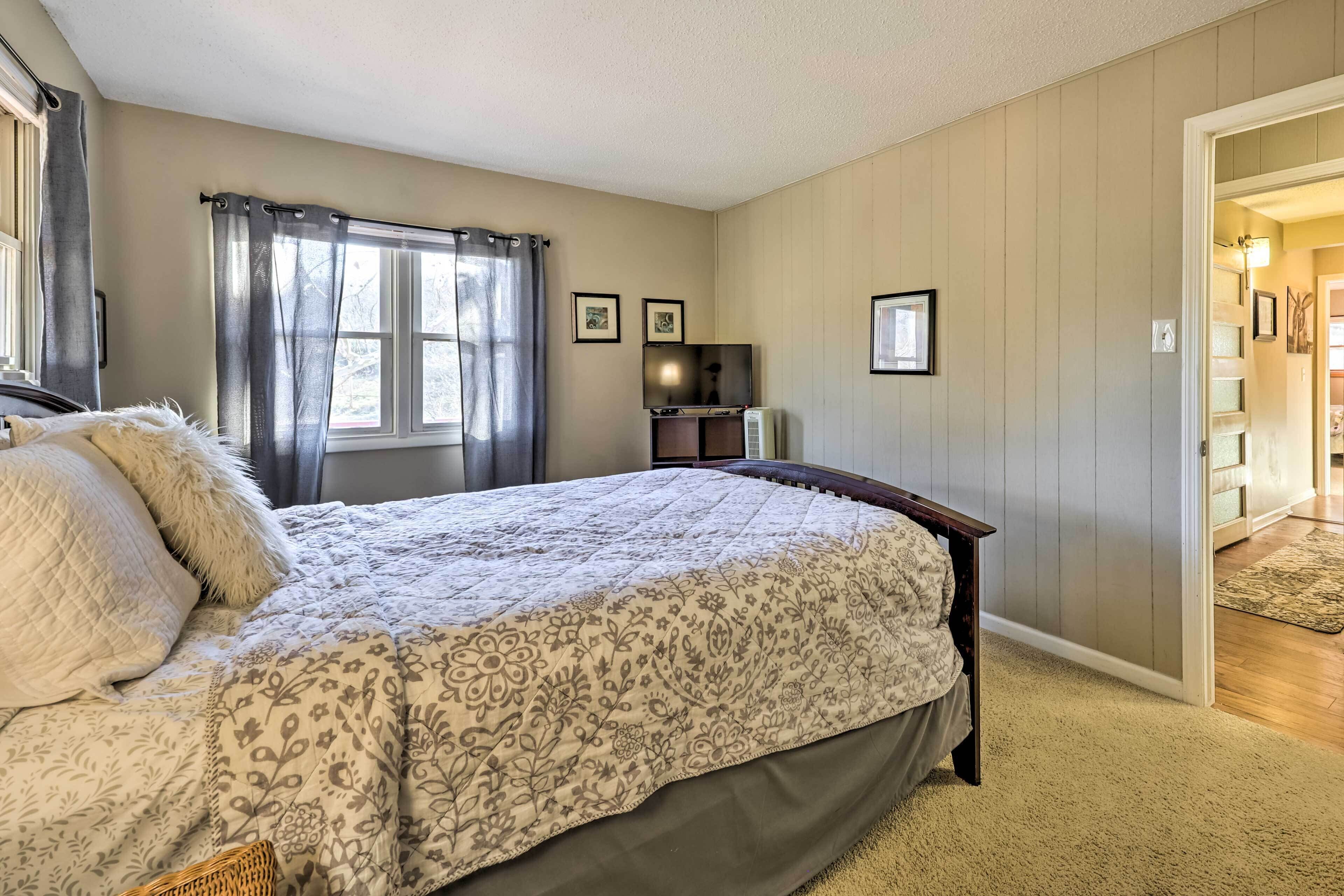 A bedroom with a large bed, a dresser, a TV, and a window with curtains.
