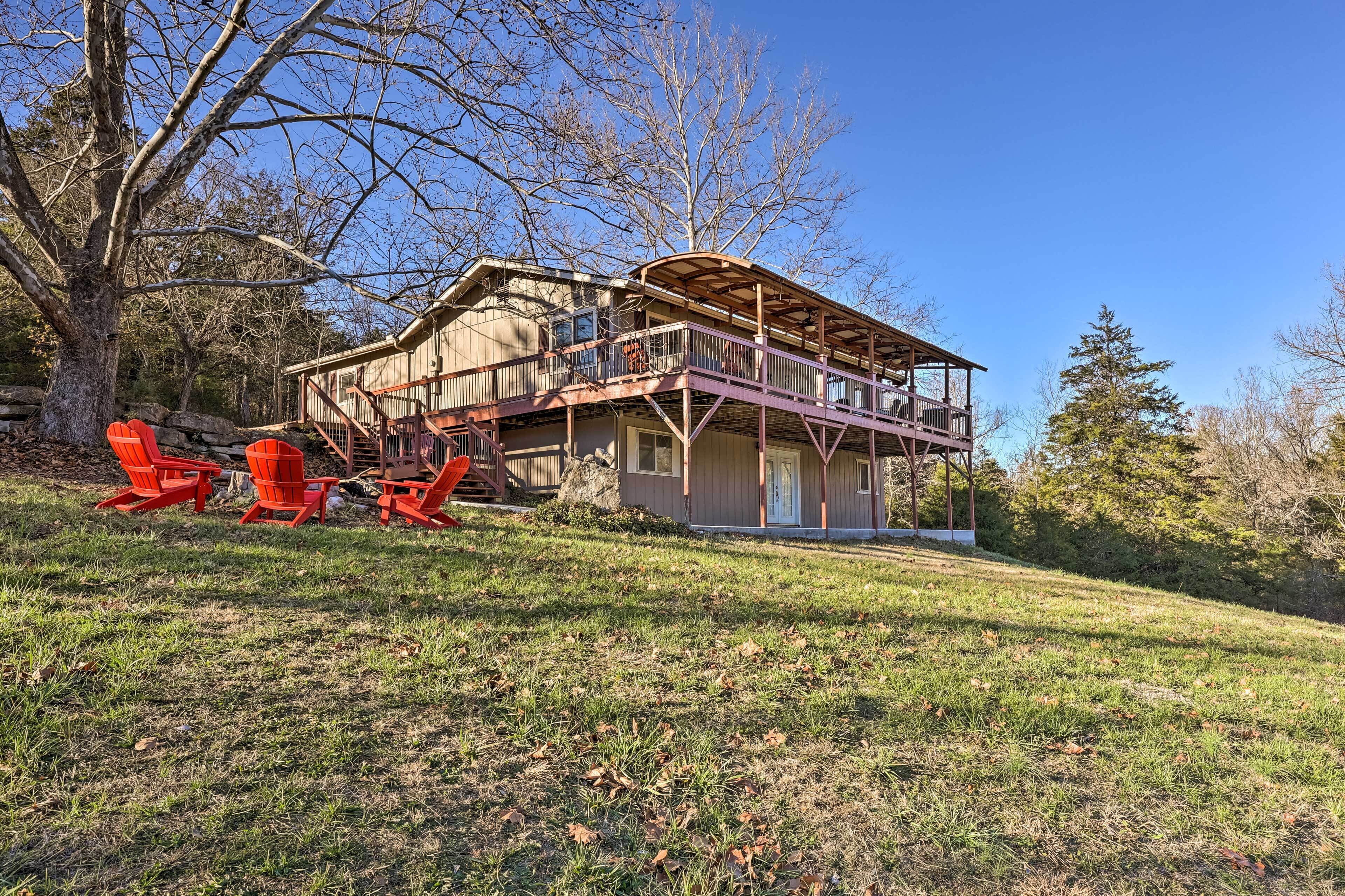 A two-story wooden house with a balcony, surrounded by trees and grass.