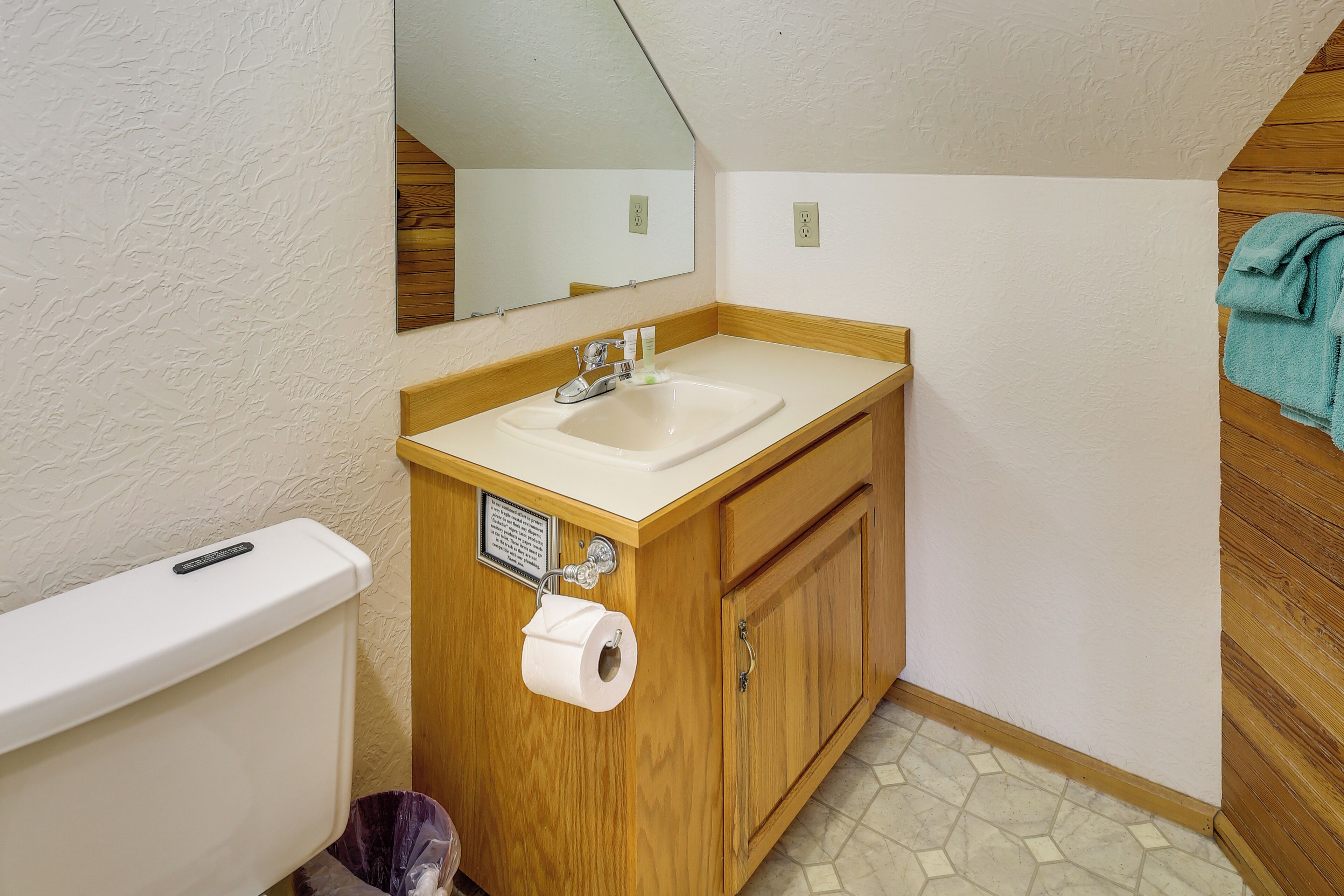 A bathroom with a wooden vanity, a white sink, a mirror, and a toilet.