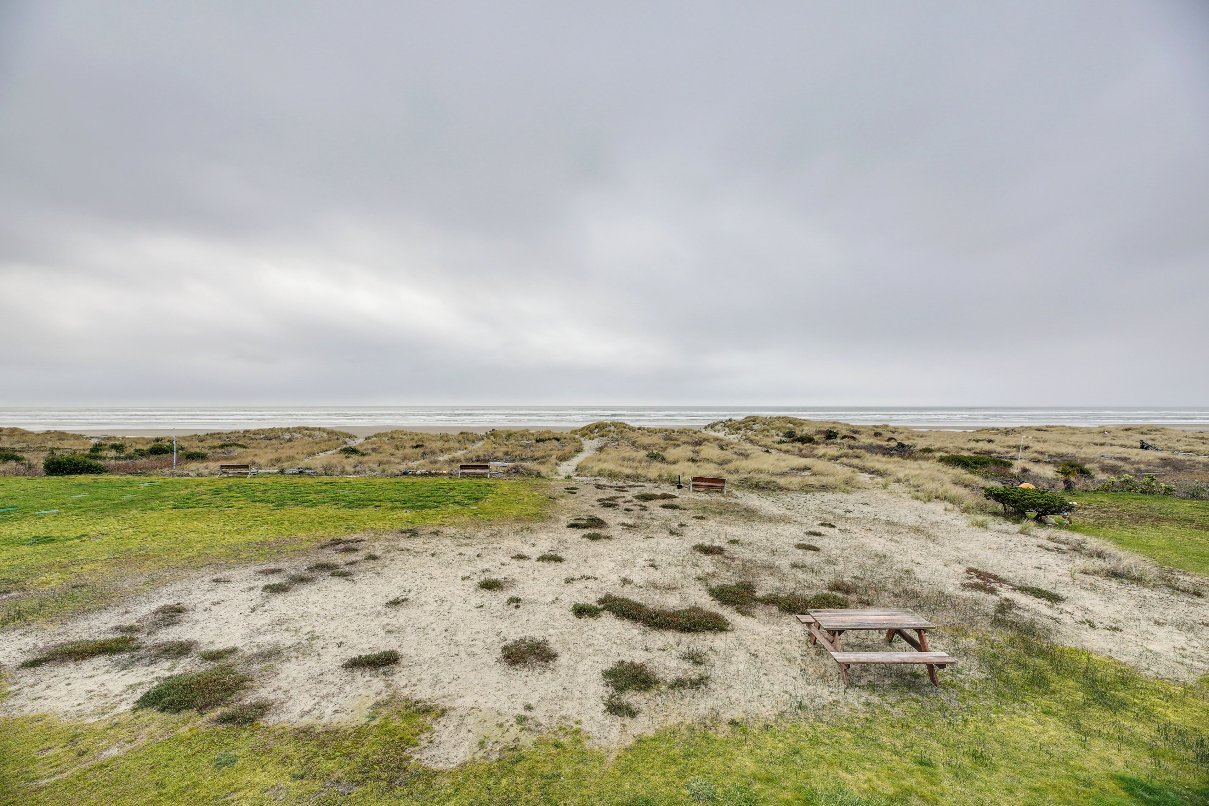 A sandy beach with a picnic table and a path leading to the water.