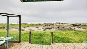 A wooden deck with a glass enclosure overlooking a grassy area with picnic tables and dunes. - Sanderling Sea Cottages, Unit 3 w/ Private Balcony (Waldport)