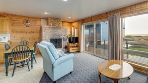 A cozy living room with a fireplace, a TV, and a dining area with wooden chairs. - Sanderling Sea Cottages, Unit 3 w/ Private Balcony (Waldport)