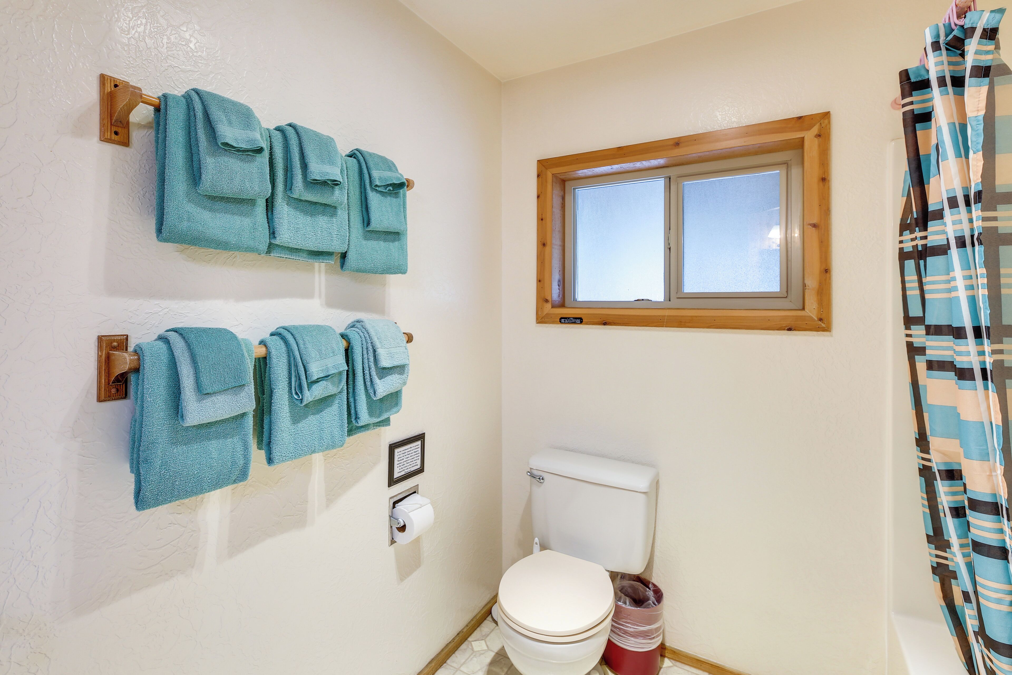 Une salle de bain avec deux porte-serviettes sur lesquels sont posées des serviettes bleues, des toilettes, une fenêtre et un rideau de douche.