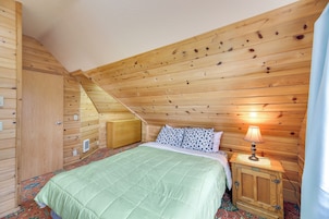 A cozy bedroom with a wooden sloped ceiling, a bed with a green quilt, a nightstand with a lamp, and a wooden wardrobe.