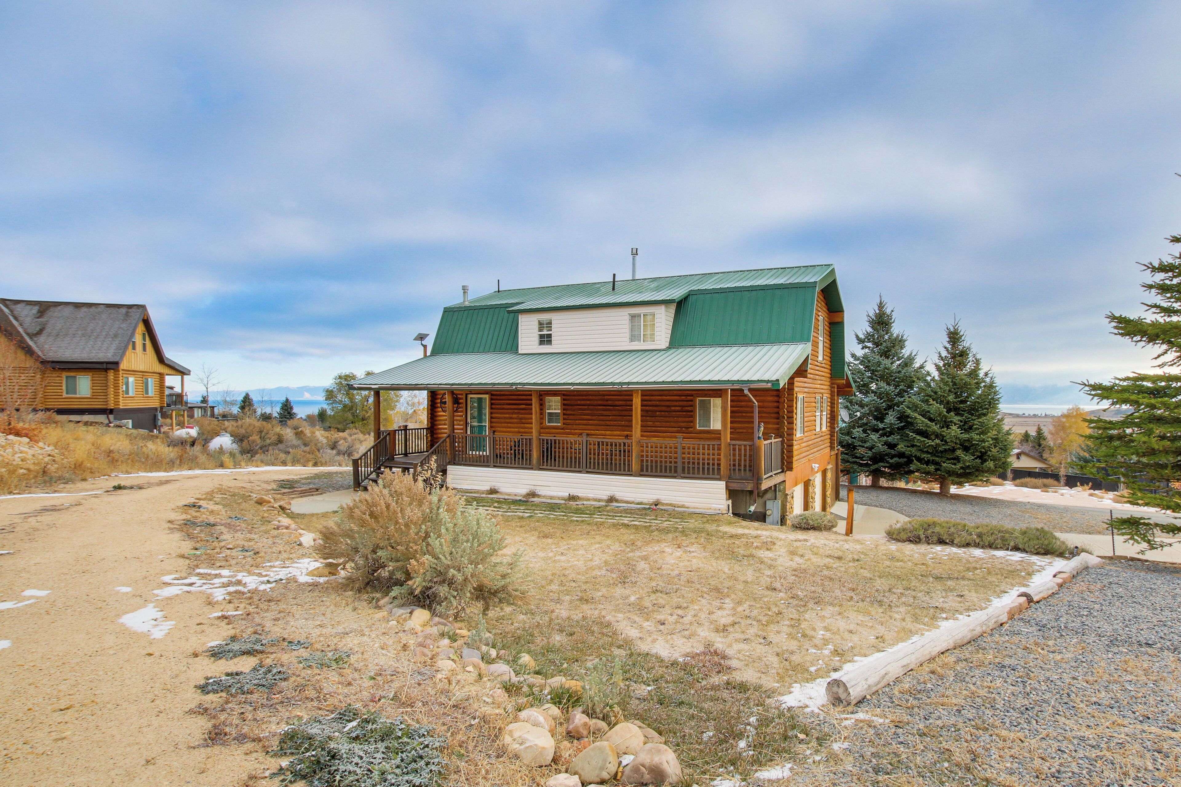A log cabin with a green roof, a porch, and a gravel driveway.