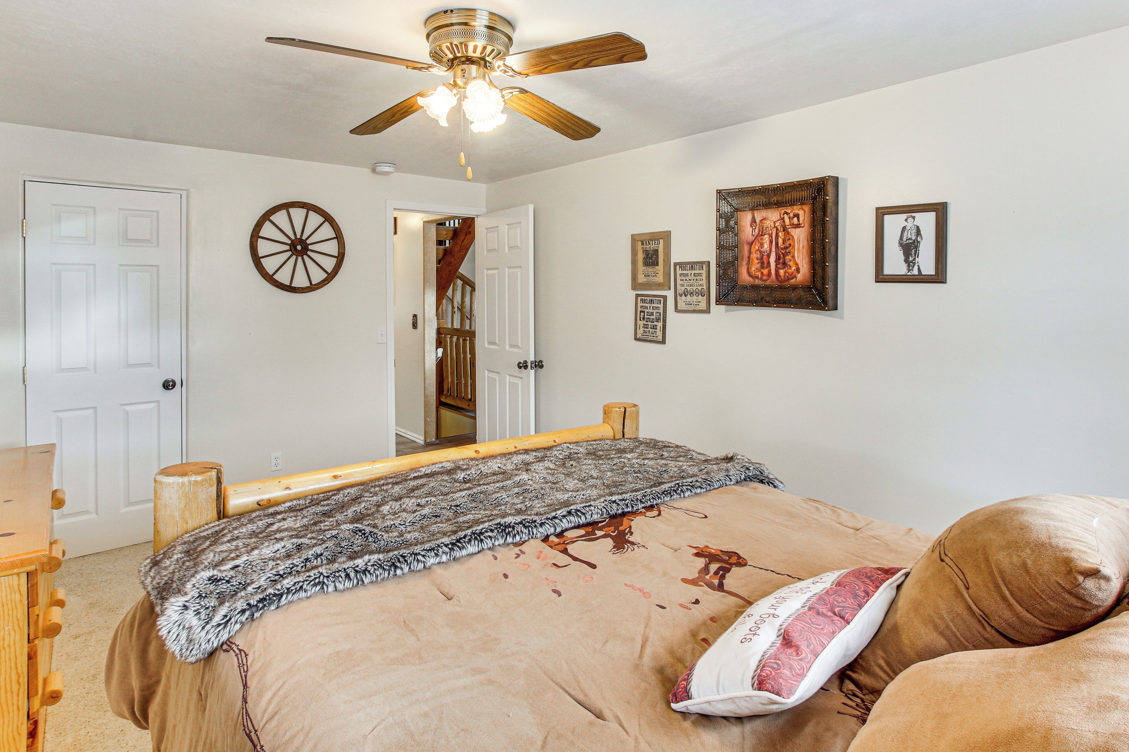 A bedroom with a bed, a ceiling fan, a wooden headboard, a wall clock, and framed pictures.