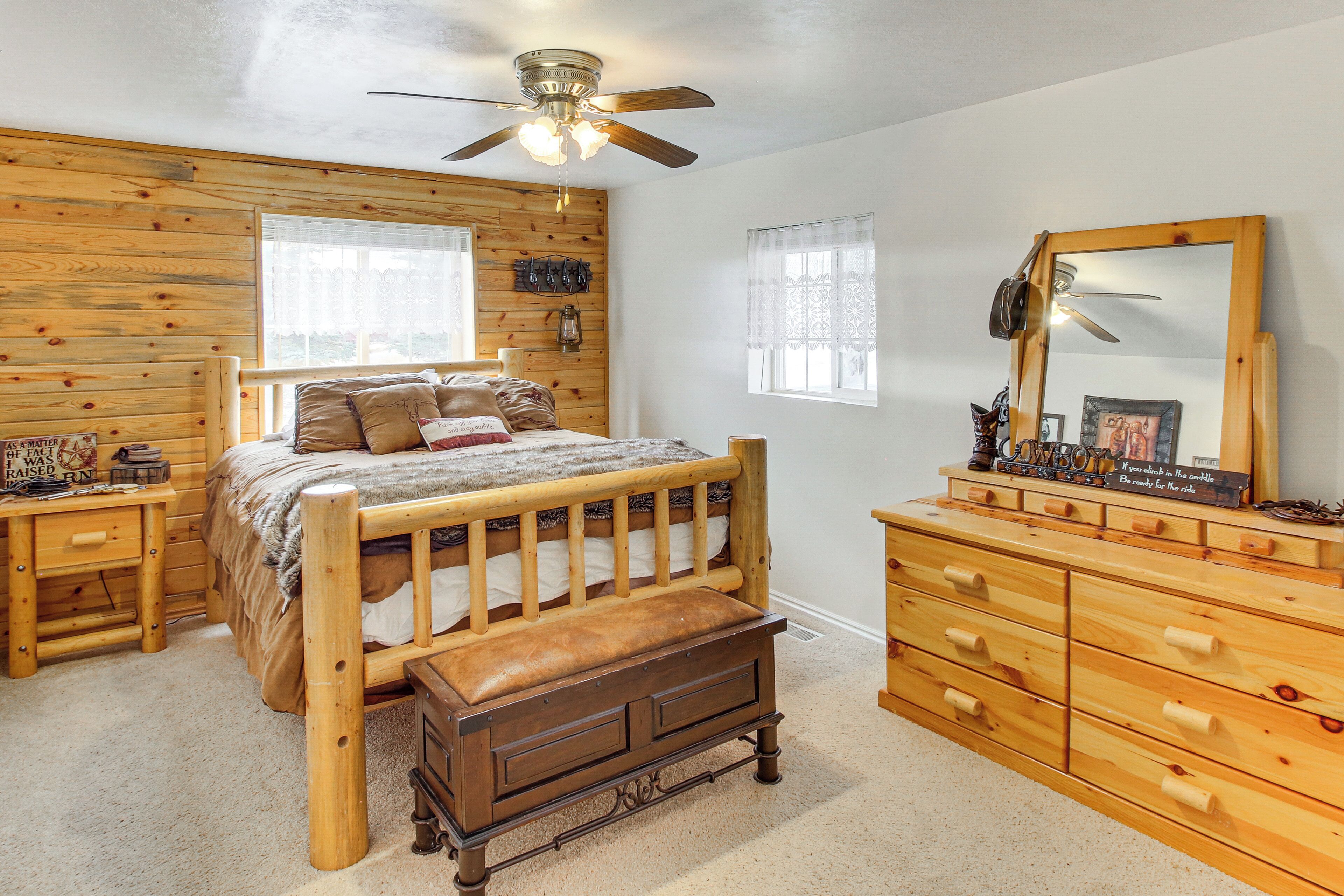 A bedroom with a wooden bed, a dresser, a mirror, and a ceiling fan.