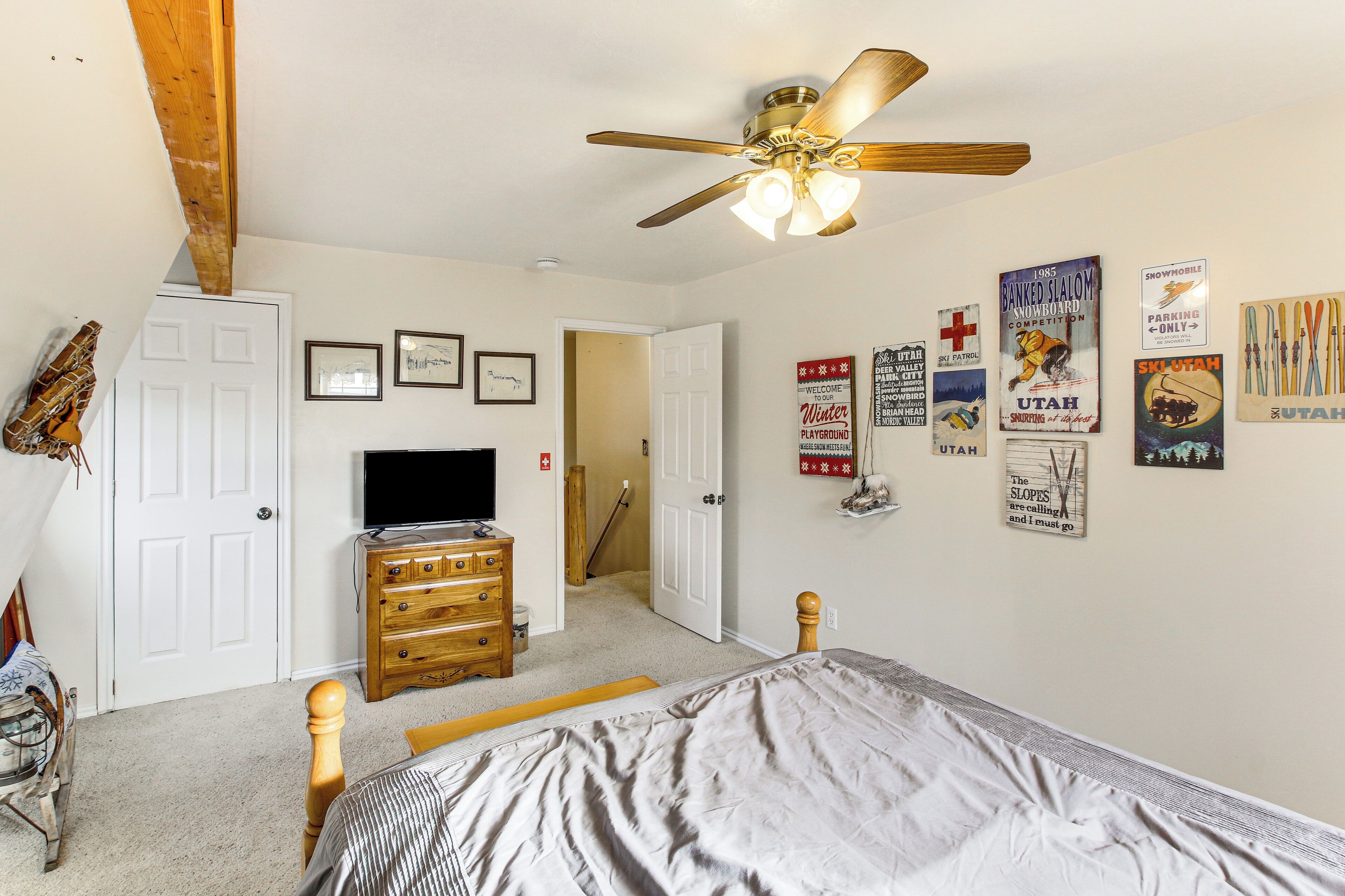 A bedroom with a bed, wooden dresser, ceiling fan, and various wall decorations including signs and framed pictures.