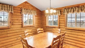 A wooden cabin interior with a dining table, chairs, and large windows.