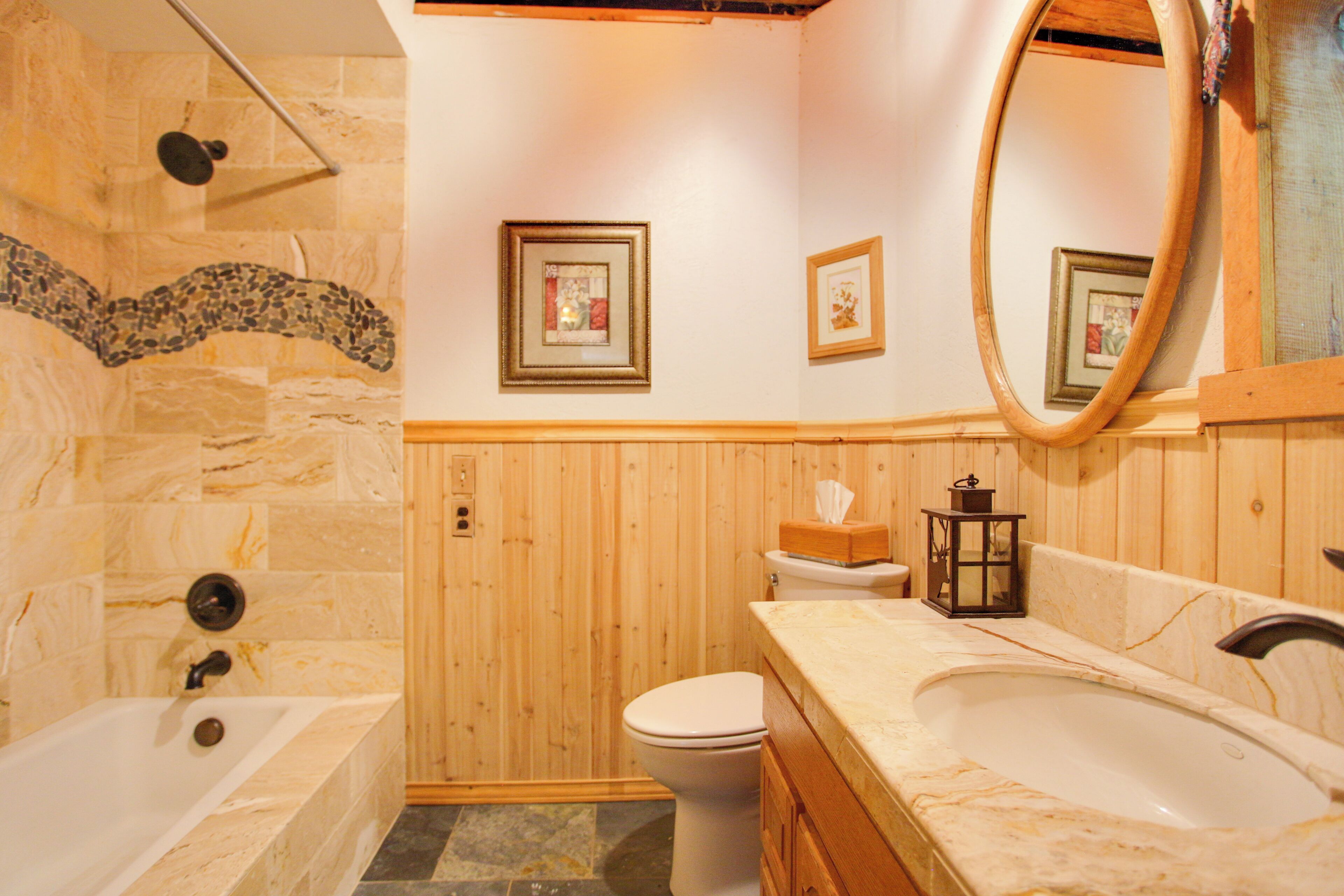 A bathroom with a stone shower, a wooden vanity, a toilet, and framed pictures on the wall.