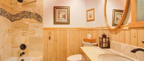 A bathroom with a stone shower, a wooden vanity, a toilet, and framed pictures on the wall.