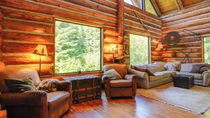 A cozy log cabin interior with a fireplace, leather sofas, and large windows offering a forest view. - Cozy Easton Cabin w/ Wenatchee Nat'l Forest Views! (Easton)