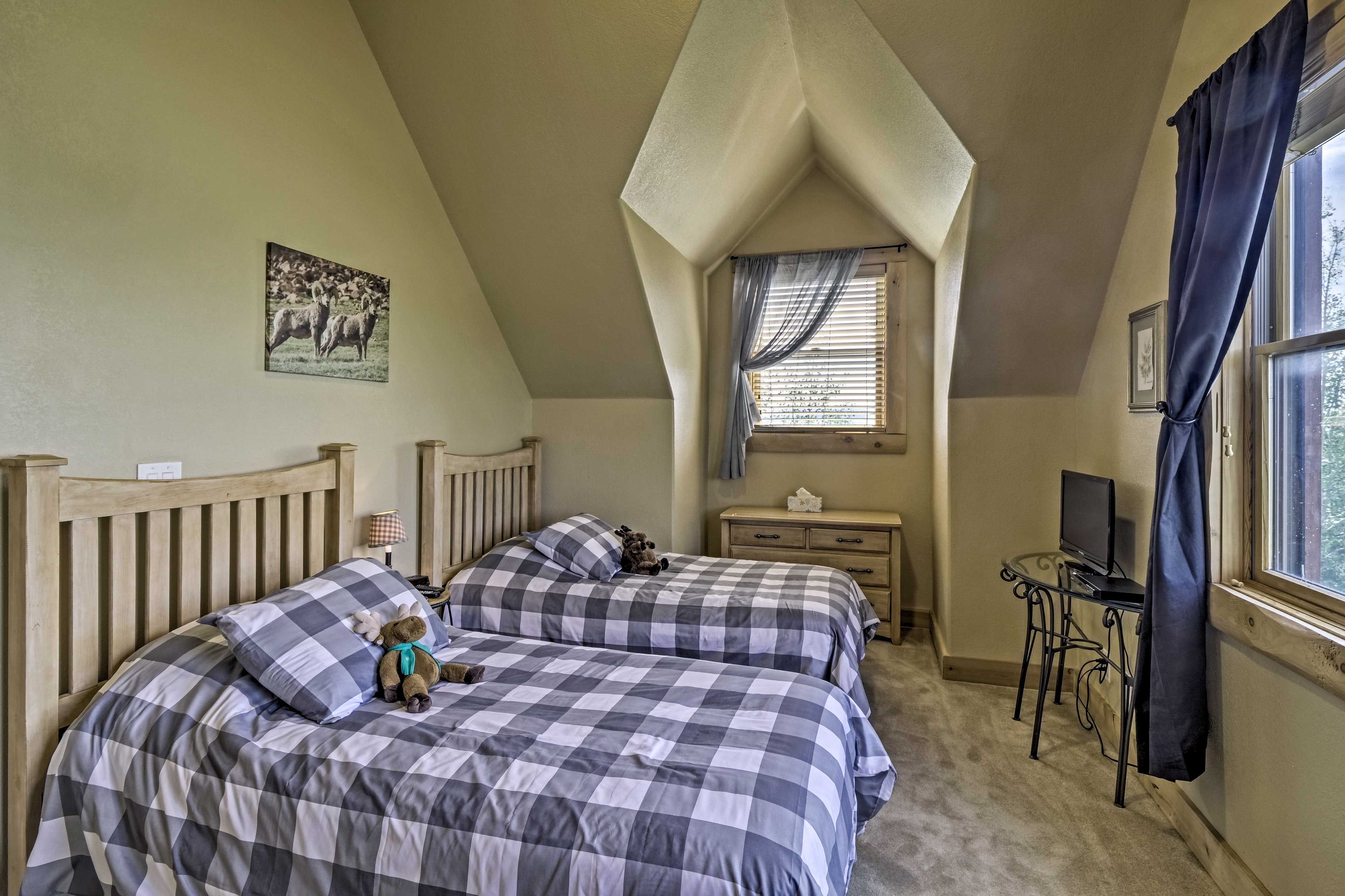 A bedroom with two beds, a desk, a TV, and a window with curtains.