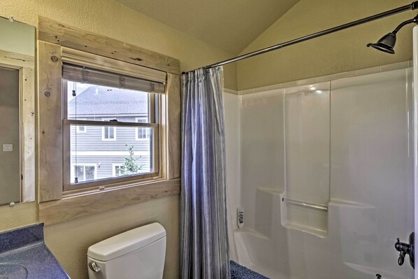 Une salle de bain avec des toilettes, une douche, une fenêtre et un rideau.