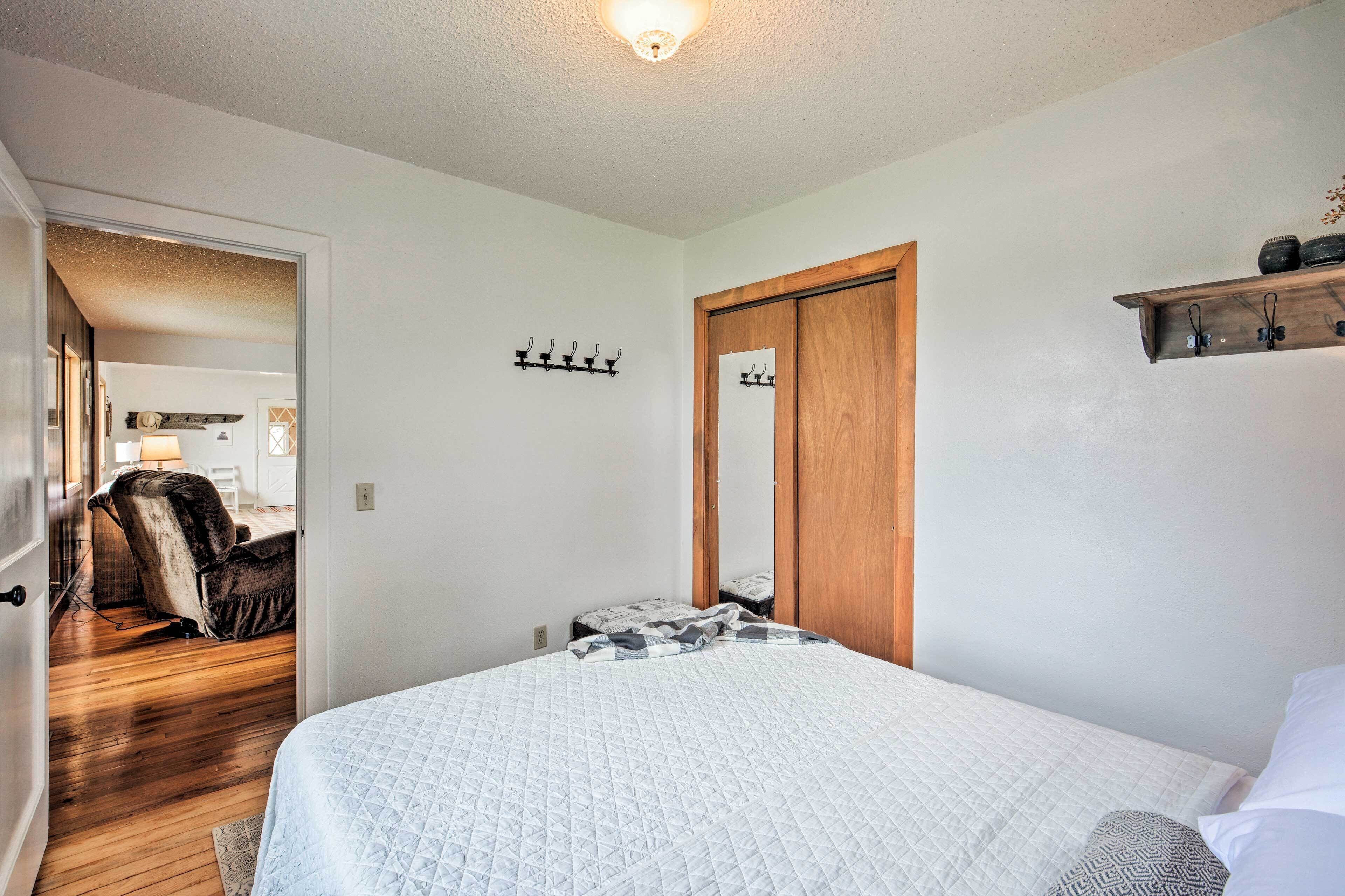 Un dormitorio con una cama, una puerta de madera, un perchero y un pasillo que lleva a otra habitación.