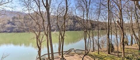 A wooden deck with a railing overlooking a calm lake, surrounded by trees and a hilly landscape.
