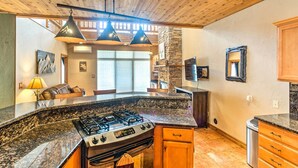 Una cocina con encimeras de granito, estufa a gas, armarios de madera e iluminación colgante.
