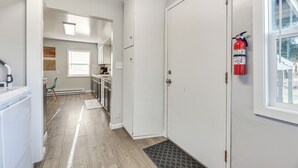 Un couloir étroit avec une porte blanche, un extincteur fixé au mur et une fenêtre sur la droite.