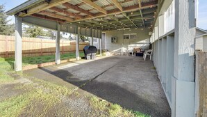 Un patio couvert équipé d’un barbecue, de mobilier d’extérieur et d’une clôture en bois en arrière-plan.