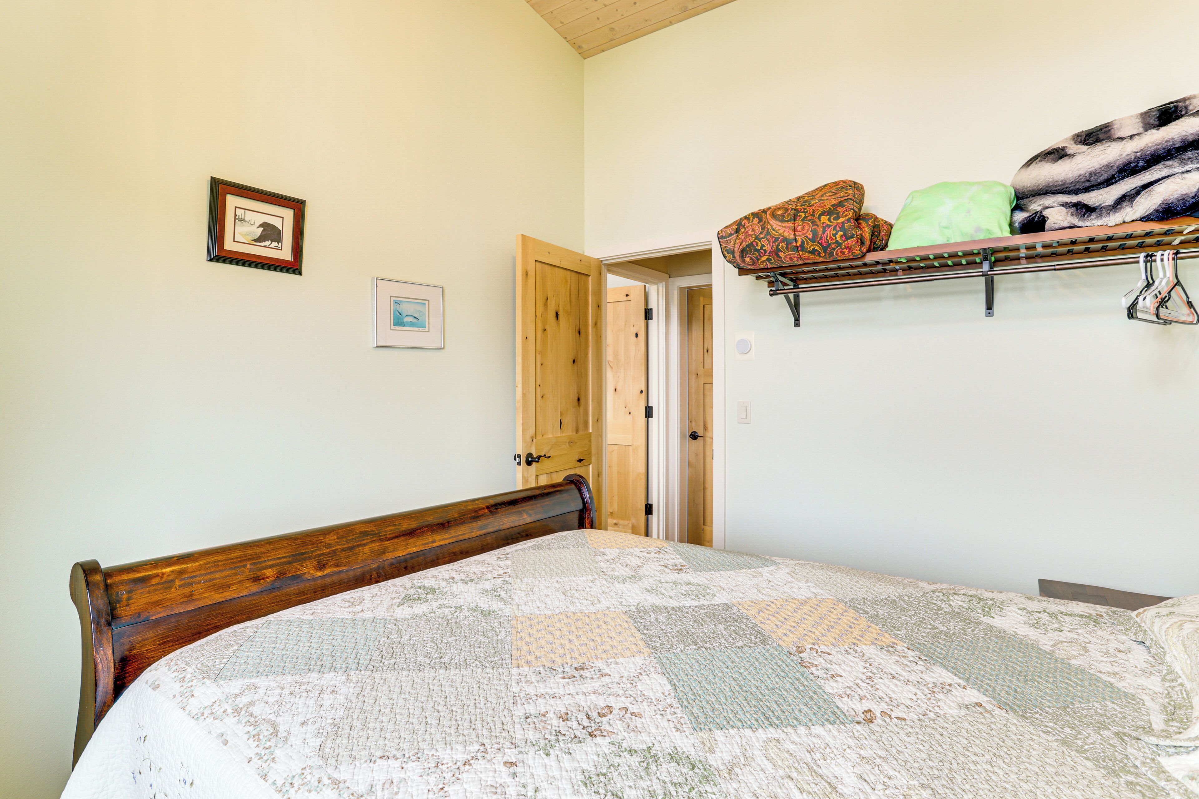 Une chambre à coucher avec un lit en bois, une courtepointe, une étagère avec des couvertures pliées et une porte donnant sur une autre pièce.